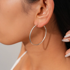 Side view of a model wearing large silver hoop earrings with a high-polished finish