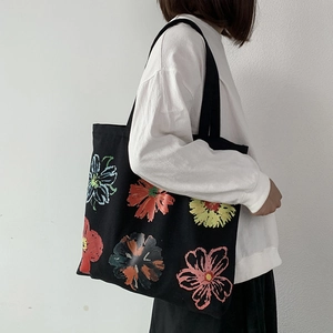 Canvas tote bag in black with vibrant floral print shown on person in casual style