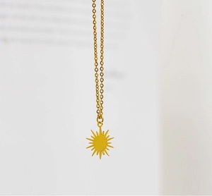 Macro detail of 18K gold plated sun and star pendant necklace on minimalist background