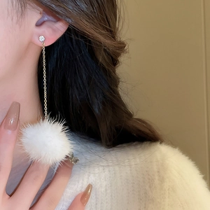 Close-up of elegant long drop earrings with white mink fur balls and gold chain details