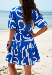 Rear view of a blue and white geometric print dress featuring waist tie and ruffle hem at beach
