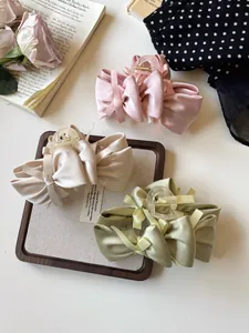 Close-up of pink, beige, and green satin bow hair claws on a decorative wooden tray
