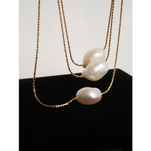 Golden irregular baroque pearl necklace with three pearls on a black velvet display stand
