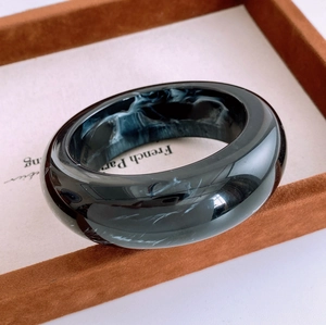 Detail view of wide black resin bangle with white marble texture on jewelry display