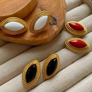 Detail of gold braided earrings with inlaid white, red, and black oval stones