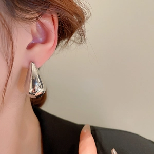 Close-up of a silver teardrop earring with high-polish metallic finish on a model