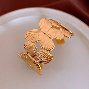 Detail of gold butterfly cuff bracelet with textured wings on a white surface