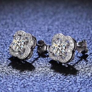 Macro shot of silver four-leaf clover moissanite earrings with halo setting on blue background
