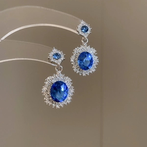 Macro detail of luxury halo stud earrings with deep blue oval gemstones and sparkling diamonds