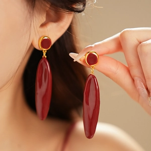 Détail de boucles d'oreilles pendantes ovales rouge foncé avec accents dorés portées