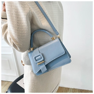 Detail of light blue crossbody bag with golden buckle on a model wearing white outfit