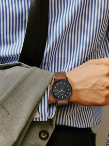 Detail of TOMI watch showing black dial with date window and brown leather strap