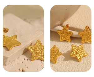 Detail of star-shaped gold earrings with lava texture on beige travertine base