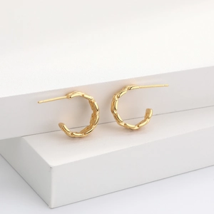 Detail view of gold braided C-shaped hoop earrings on a minimalist white display
