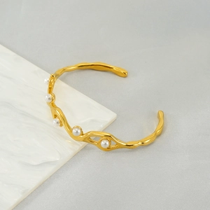 Detail of a gold-plated open bangle featuring delicate white pearls on a marble surface
