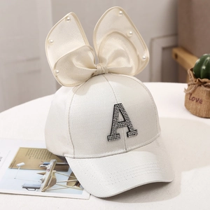 Detail of cream baseball cap featuring pearl bow and rhinestone letter A ornament