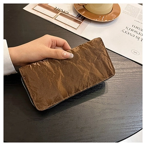 Detail of a brown long zip wallet with unique wrinkled paper texture held over a desk