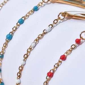 Detail of bohemian gold chain with blue white red enamel beads and charm elements