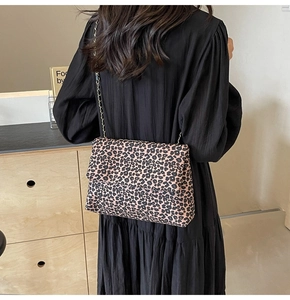 Detail of leopard print tote bag with gold chain strap worn over a black dress
