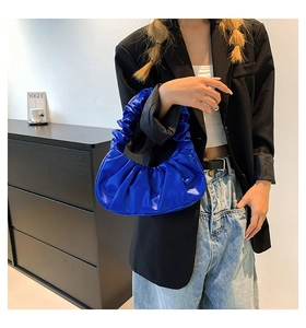 Model wearing a stylish blue ruched leather crescent bag in a minimalist studio setting