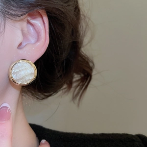 Dettaglio macro dell'orecchino placcato oro 16K con disco bianco e cornice ondulata