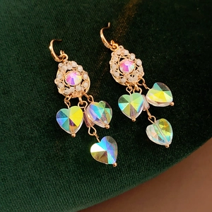 Macro shot of vintage gold drop earrings with heart rainbow crystals on green velvet