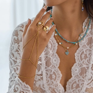 Detail of gold-plated turquoise hand chain featuring heart and hand charm rings