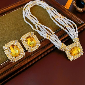 Dettaglio di un set di gioielli d'oro quadrati con gemme gialle e collana di perle