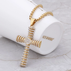 Iced out gold cross pendant necklace with box chain draped on white ceramic cup