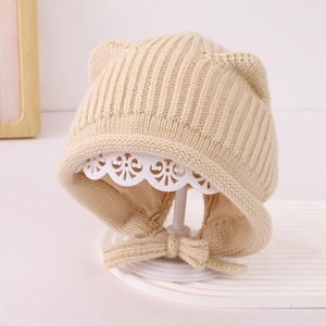 Dettaglio del cappello neonato in maglia beige con orecchie e lacci su supporto bianco