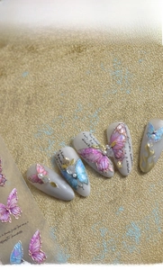Detailed view of 3D butterfly nail charms with metallic edges and pearl accents