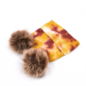 Détail du bonnet en maille tie-dye avec deux pompons en fausse fourrure et revers côtelé