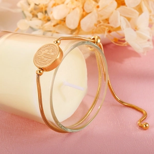 Detailed close-up of a gold snake chain bracelet with Saint Benedict medal on a candle cup