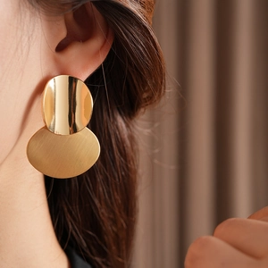 Close-up of golden oval brushed metal pendant earrings worn by a female model
