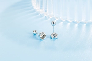 Detail of silver stud earrings with round zircon and spherical screw back on blue background