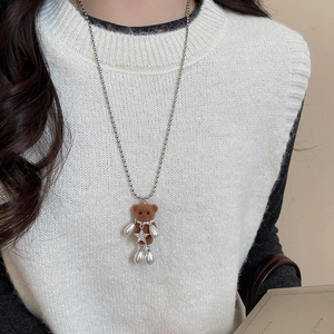 Close-up of a brown flocked bear necklace with white pearls on a white knit vest