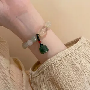 Detail of beaded bracelet with green jade-style beads and a red lucky charm on wrist