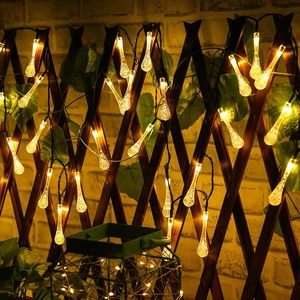 Detail of warm yellow solar bubble teardrop lights on a wooden fence with green leaves