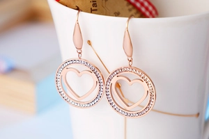 Detailed macro of rose gold heart earrings with zircon studs on a porcelain cup edge