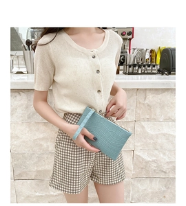 Detail view of light blue crocodile embossed clutch bag held by a model in a warm setting
