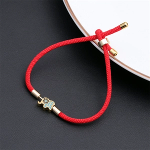 Macro detail of red woven rope bracelet featuring a gold elephant charm with blue crystals