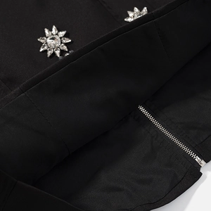 Détail d'une robe noire avec fermeture éclair métallique et ornement soleil en cristal