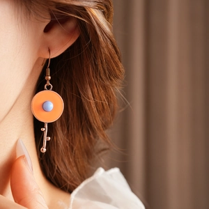 Detailed view of vintage orange round earrings with blue bead worn by a model