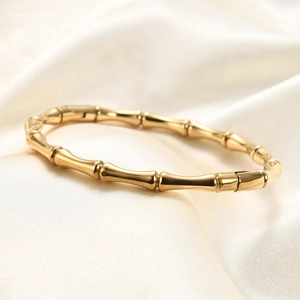 Polished gold bamboo joint bangle in stainless steel with magnetic closure on white silk