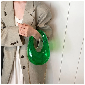 Close-up of green transparent acrylic U-shape handbag with gold chain strap on model