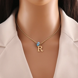 Detail of gold necklace featuring letter R pendant and small blue bead on model