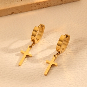 Détail de boucles d'oreilles créoles dorées avec pendentifs croix sur cuir