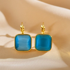 Close-up of golden stainless steel hoop earrings with faceted blue square gemstones