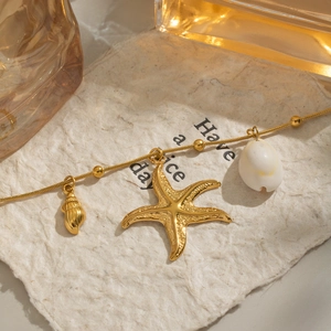 Detail of gold starfish and shell charms on a snake chain necklace over warm lighting