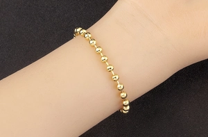 Detail of 18k gold plated ball chain bracelet showing high-polish finish on black background